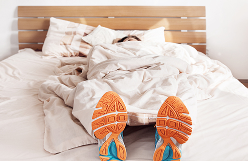 Runner in bed wearing shoes | Fatigue Science